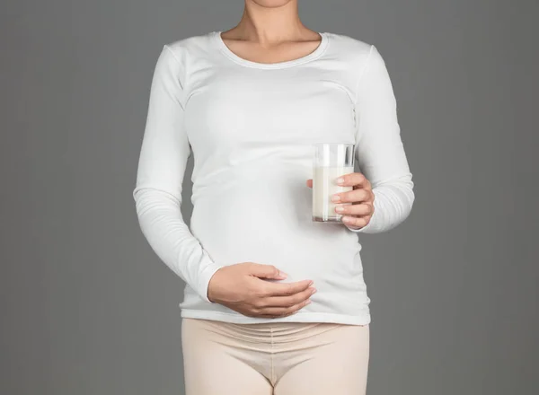 Young pregnant woman holding a glass of milk Isolated on grey ba — Stock Photo, Image
