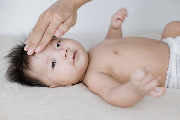 Новорожденная лежит в постели, а мать касается ее лба.