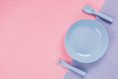 Blue plastic plate with spoon and fork on pink background