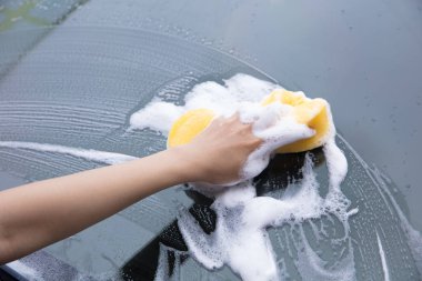 Sarı sünger köpüklü bir arabanın ön camını temizlemek.