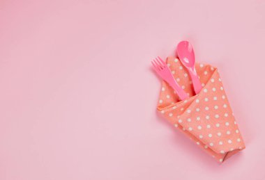 Plastic spoon, fork and pink polka dot cloth napkin on pink back