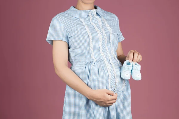Pregnant woman in Blue Shirt Dress holding baby crochet boots is — 图库照片