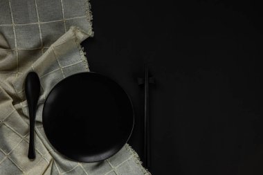 Set black plate with spoon and chopsticks on black background