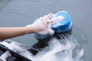 Mavi sünger köpüklü bir arabanın ön camını temizlemek.