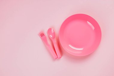 Pink plastic plate with spoon and fork on pink background