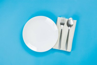 A white plate with spoon and fork on blue background
