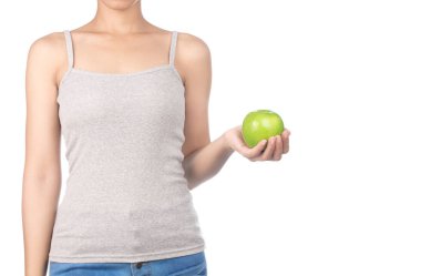 Gri kolsuz tişörtlü ve kot pantolonlu bir kadın yeşil elma tutuyor.