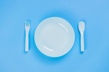 Blue plastic plate with spoon and fork on blue background