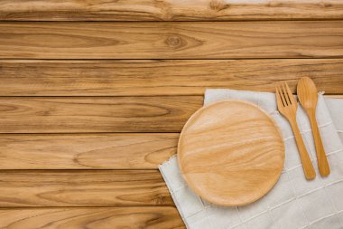 A wood plate rests on a white cloth. There are spoon and fork on