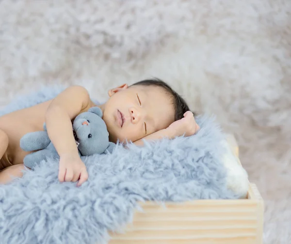 Petit bébé endormi embrassant un ours dans une boîte en bois. — Photo