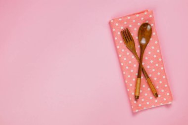 wood spoon, fork and pink polka dot cloth napkin on pink backgro