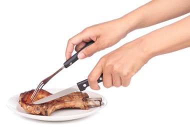 İnsan elleri beyaz arka planda izole edilmiş çatal ve bıçakla lezzetli barbekü kaburgaları kesiyor.