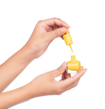 Beyaz arka planda sarı tırnak cilası şişesini tutan el.