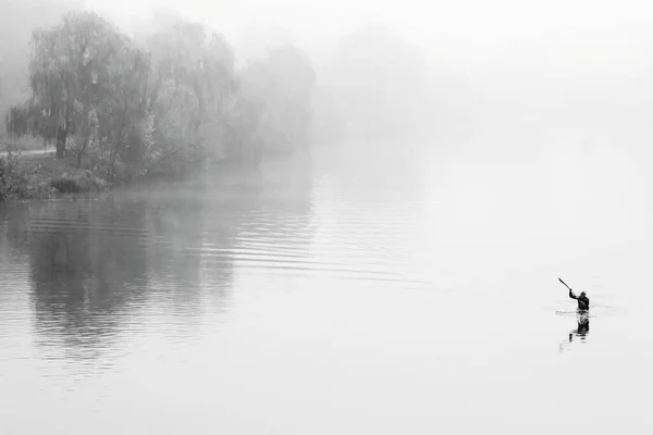 Man on kayak in fog. Black and white photo. Autumn mystic landscape with boat on foggy river