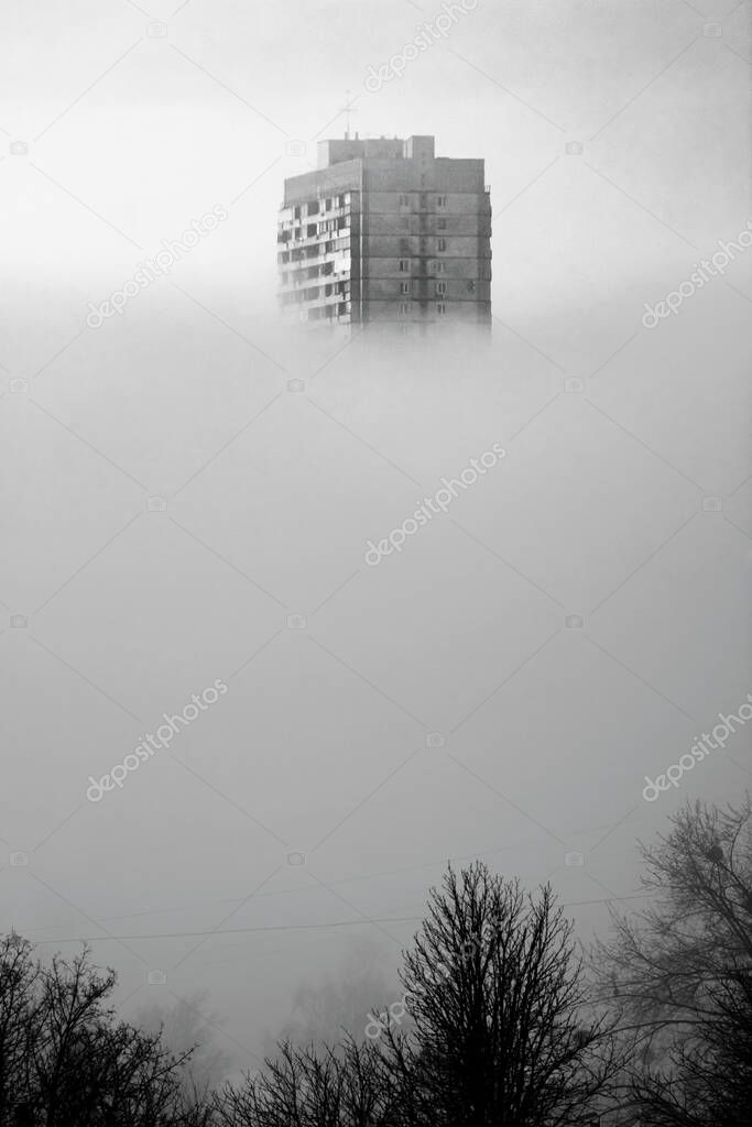 High-rise building above clouds. Black and white photo. City landscape  in morning fog