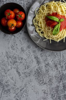 Domates ve fesleğen soslu ev yapımı spagetti, yukarıdan gri arka planda görünüyor. İtalyan pastası. Düz yatıyordu..