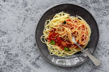 Domates ve fesleğen soslu ev yapımı spagetti, yukarıdan gri arka planda görünüyor. İtalyan pastası. Düz yatıyordu..