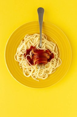 Domates ve fesleğen soslu ev yapımı spagetti, sarı arka planda yukarıdan görülüyor. İtalyan pastası. Düz yatıyordu..