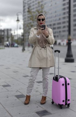 Başörtüsü ve bavulu olan çekici bir Arap kadın telefonda konuşuyor.