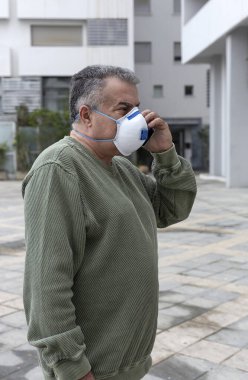 Koronavirüs salgını için koruyucu maskeli yetişkin bir adam cep telefonuyla konuşuyor.