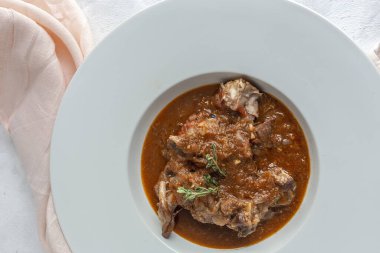 Geleneksel ev yapımı kuzu güveci, beyaz arka planda yukarıdan bakıldığında aromatik bitkilerle bezenmiş. Üst görünüm