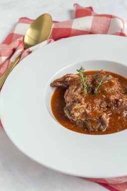 Geleneksel ev yapımı kuzu güveci, beyaz arka planda yukarıdan bakıldığında aromatik bitkilerle bezenmiş. Üst görünüm