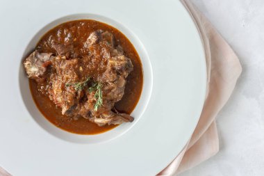 Geleneksel ev yapımı kuzu güveci, beyaz arka planda yukarıdan bakıldığında aromatik bitkilerle bezenmiş. Üst görünüm