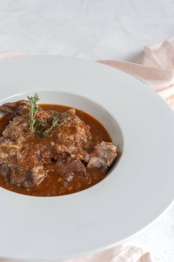 Geleneksel ev yapımı kuzu güveci, beyaz arka planda yukarıdan bakıldığında aromatik bitkilerle bezenmiş. Üst görünüm