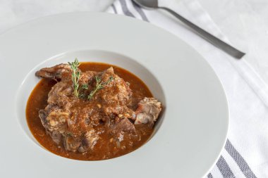 Geleneksel ev yapımı kuzu güveci, beyaz arka planda yukarıdan bakıldığında aromatik bitkilerle bezenmiş. Üst görünüm