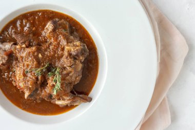 Geleneksel ev yapımı kuzu güveci, beyaz arka planda yukarıdan bakıldığında aromatik bitkilerle bezenmiş. Üst görünüm