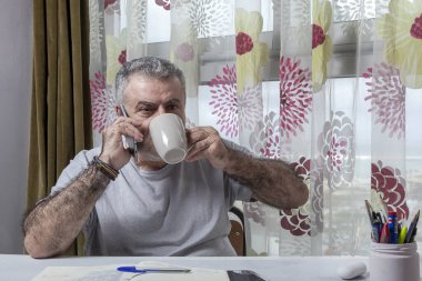 Evde pijama, dizüstü bilgisayar ve cep telefonu Coronavirus konseptiyle çalışan sakallı olgun bir adam.