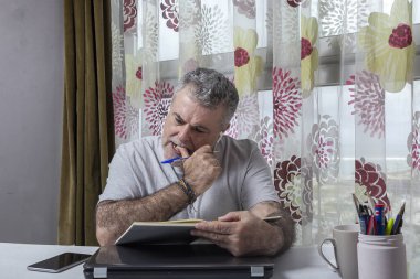 Evde pijama, dizüstü bilgisayar ve cep telefonu Coronavirus konseptiyle çalışan sakallı olgun bir adam.