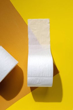Beyaz tuvalet kağıdı renkli arka planda yuvarlanıyor. Güneş ışığı yukarıdan geliyor. Düz manzara.