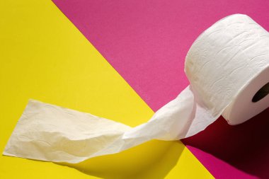 Beyaz tuvalet kağıdı renkli arka planda yuvarlanıyor. Güneş ışığı yukarıdan geliyor. Düz manzara.