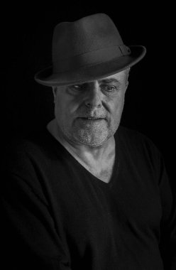 Koyu arkaplanda klasik şapka ve sakallı olgun bir adamın dramatik portresi.