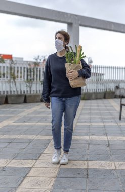 Karantina sırasında koronavirüse karşı koruyucu maskeli olgun bir kadın gerekli ürünleri satın alarak evine dönüyor. Covid-19 konsepti.