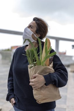 Karantina sırasında koronavirüse karşı koruyucu maskeli olgun bir kadın gerekli ürünleri satın alarak evine dönüyor. Covid-19 konsepti.