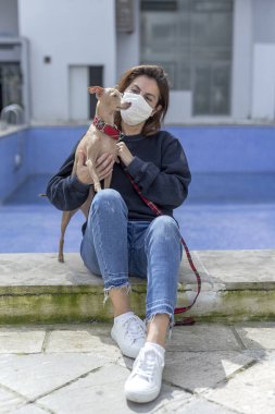 Karantina sırasında koronavirüse karşı koruyucu maskeli bir kadın boş havuzlu bir şehirde köpekle oynuyor. Covid-19 konsepti