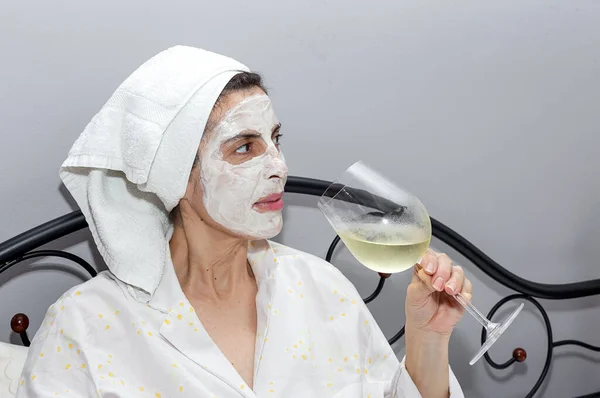 熟女はベッドでフェイスマスクで彼女の顔を世話します Covid 19隔離中にワインのグラスを飲みます コロナウイルスの概念 — ストック写真
