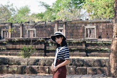 Beyaz şapkalı ve çizgili gömlekli genç Asyalı kadın Hindu tapınağında poz veriyor. Prasat Hin Phanom Rung, Tayland