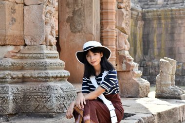Çizgili elbiseli ve beyaz şapkalı güzel Asyalı kız eski bir Hindu tapınağının temelinde oturuyor. Prasat Hin Phanom Rung, Tayland