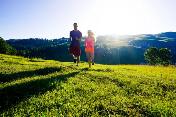 Running fitness couple of runners doing sport on road outdoor. Active living man and woman jogging training cardio in summer outdoors nature.