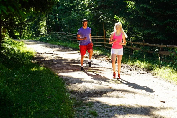 Running fitness couple of runners doing sport on road outdoor. Active living man and woman jogging training cardio in summer outdoors nature.