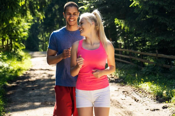 Running fitness couple of runners doing sport on road outdoor. Active living man and woman jogging training cardio in summer outdoors nature.