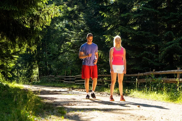 Running fitness couple of runners doing sport on road outdoor. Active living man and woman jogging training cardio in summer outdoors nature.