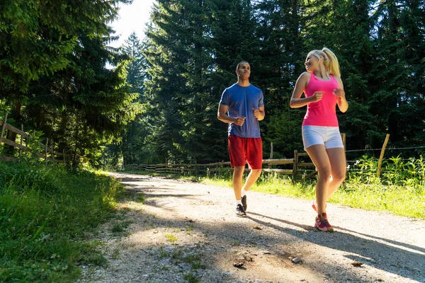Running fitness couple of runners doing sport on road outdoor. Active living man and woman jogging training cardio in summer outdoors nature.