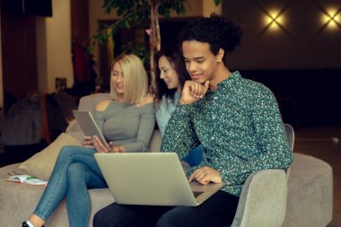 Üniversite öğrencileri, kitaplar ve dizüstü bilgisayarlarla aynı masada oturuyorlar. Üniversite kütüphanesinde bir grup çok ırklı insan..