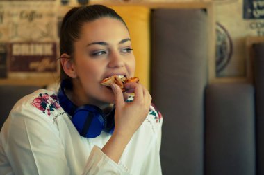 Image of happy woman while sitting in cafe and listening music and eating pizza