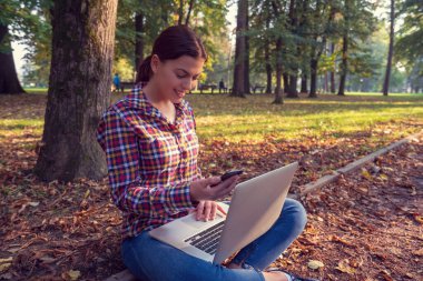 Güzel bir iş kadını, dizüstü bilgisayarlı, telefonla konuşan ve kredi kartı tutan.