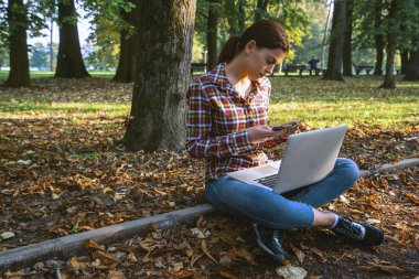 Güzel bir iş kadını, dizüstü bilgisayarlı, telefonla konuşan ve kredi kartı tutan.